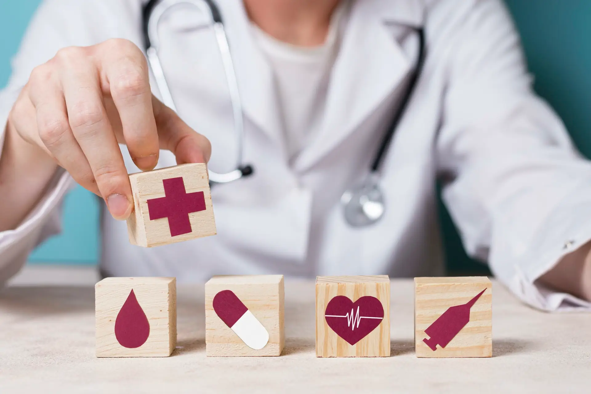 Médecin tenant un bloc en bois avec une croix rouge, à côté de blocs avec des icônes de goutte de sang, pilule, cœur et seringue.